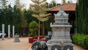 A courtyard with a stone elephant sculpture, a pagoda-style structure, and a red-roofed building. - Poojaris Niranthara Kabini (Mysore)