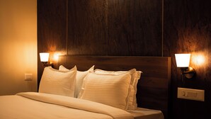 A neatly made bed with white linens in a room with wooden paneling and two wall-mounted lamps. - Poojaris Niranthara Kabini (Mysore)