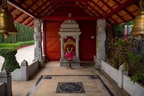 A temple with a red entrance, a central altar, and a bell in the foreground. - Poojaris Niranthara Kabini (Mysore)