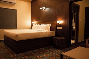 A hotel room with a large bed, bedside tables, a small cabinet, and a bathroom visible through an open door. - Poojaris Niranthara Kabini (Mysore)