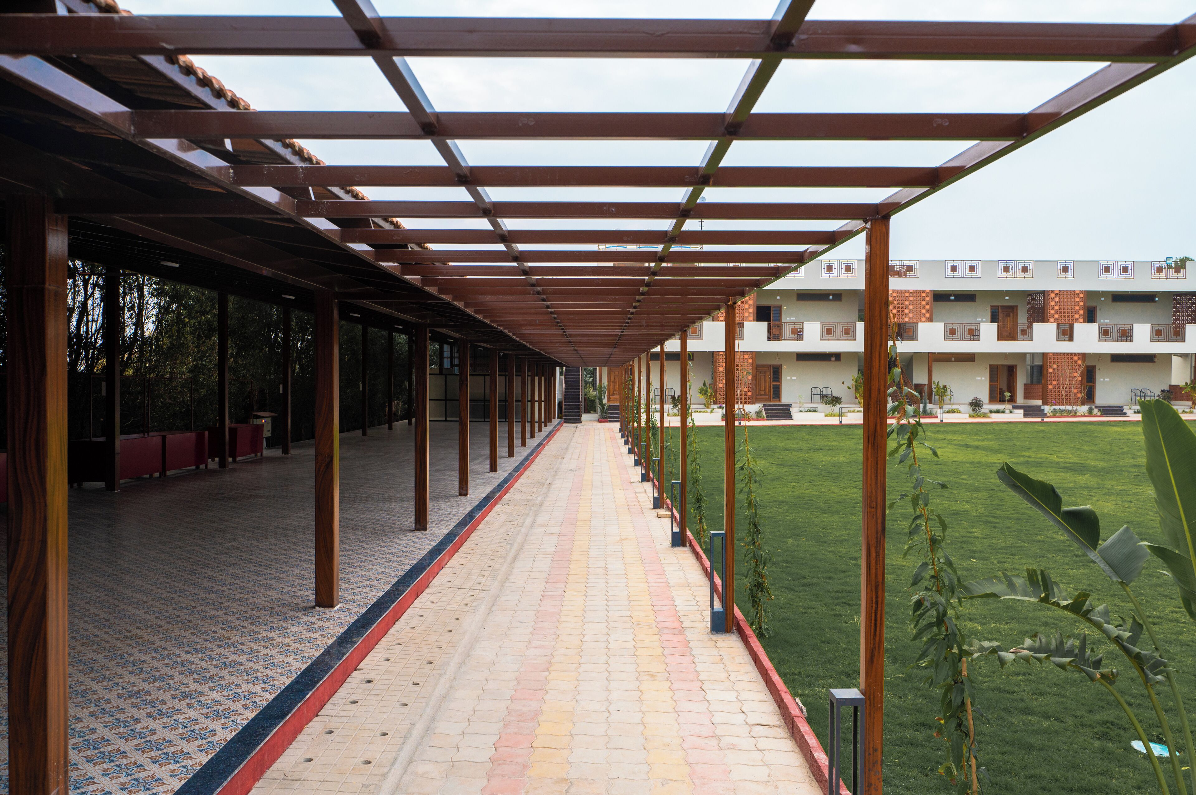 A covered walkway with a tiled floor, wooden pillars, and a view of a building with balconies.