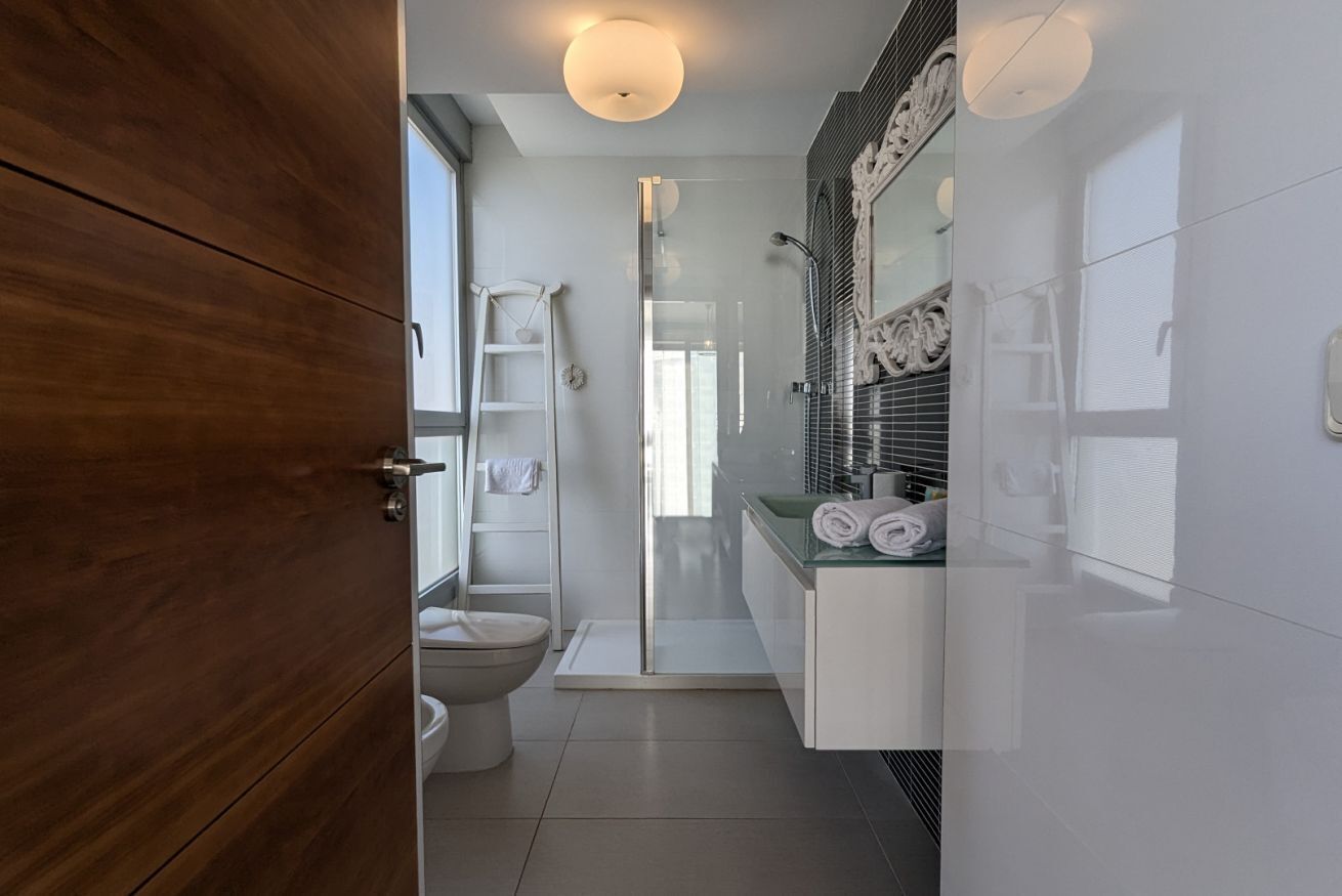 A modern bathroom with a glass shower enclosure, a toilet, and a vanity with a mirror and towel rack.