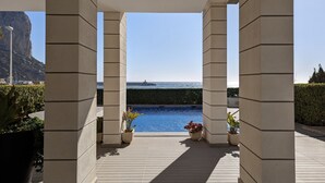 A covered outdoor area with a view of the sea and a building in the background.