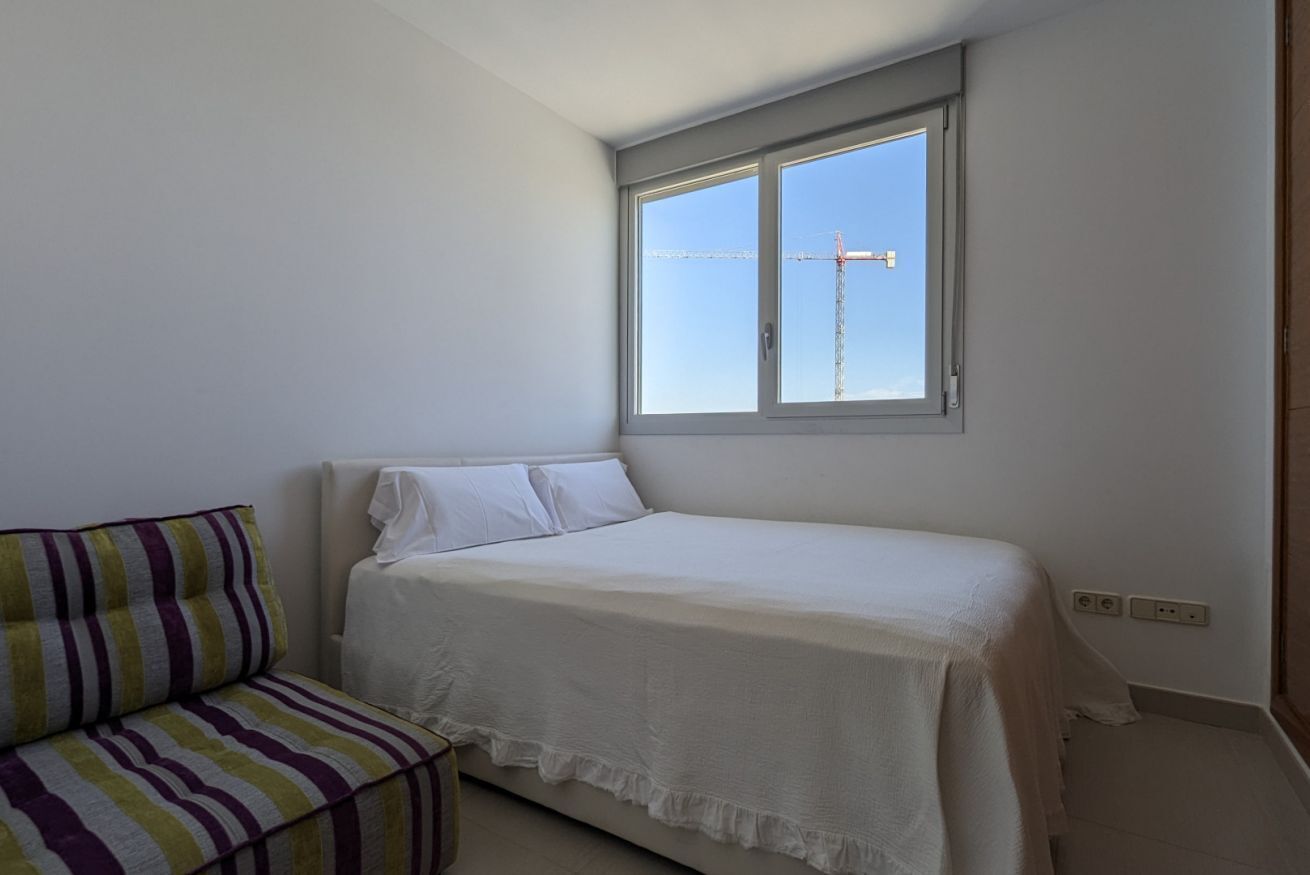 A small, neatly arranged bedroom with a single bed, a striped sofa, and a window with a view of a construction crane.
