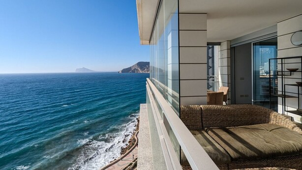 A balcony with a view of the ocean and a mountain in the distance.