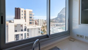 A hotel room with a large window offering a view of a coastal cityscape, including a prominent mountain and a bridge.