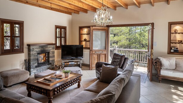 A cozy living room with a fireplace, wooden ceiling, and a balcony with a view of trees.