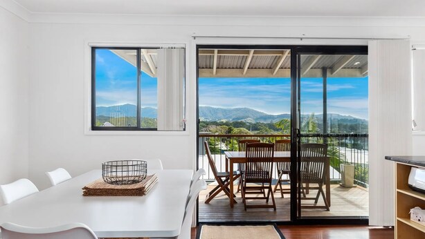 Un espace repas moderne avec une table blanche, des chaises et une vue sur les montagnes, visible à travers de grandes fenêtres.
