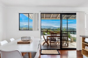 Un espace repas moderne avec une table blanche, des chaises et une vue sur les montagnes, visible à travers de grandes fenêtres.