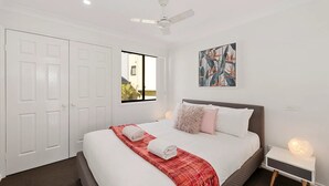 Une chambre d’hôtel avec un lit, une fenêtre, un ventilateur de plafond, une œuvre d’art murale et une table de chevet avec une lampe.