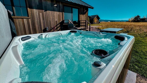 Un jacuzzi con cubierta de madera y una casa al fondo.
