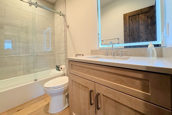 Un bagno moderno con box doccia in vetro, un water, un lavandino con specchio e mobili contenitori in legno.