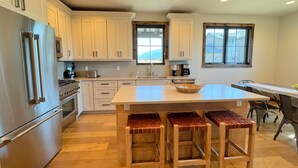 Una cocina moderna con armarios blancos, electrodomésticos de acero inoxidable, una isla grande con taburetes y una ventana con vistas a la montaña.