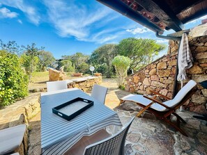 An outdoor patio with stone walls, a table with chairs, and a view of the surrounding landscape. - Domo De Chessa (San Teodoro)
