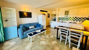 Ett kompakt bostadsutrymme med ett litet kök, en soffa, ett matbord och en TV.