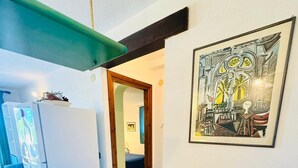 En smal hall med ett vitt kylskåp, ett grönt bord och en inramad abstrakt målning på väggen.
