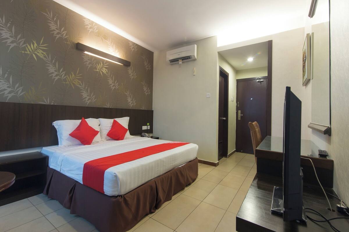 A hotel room with a bed, a desk, a television, and an air conditioning unit.