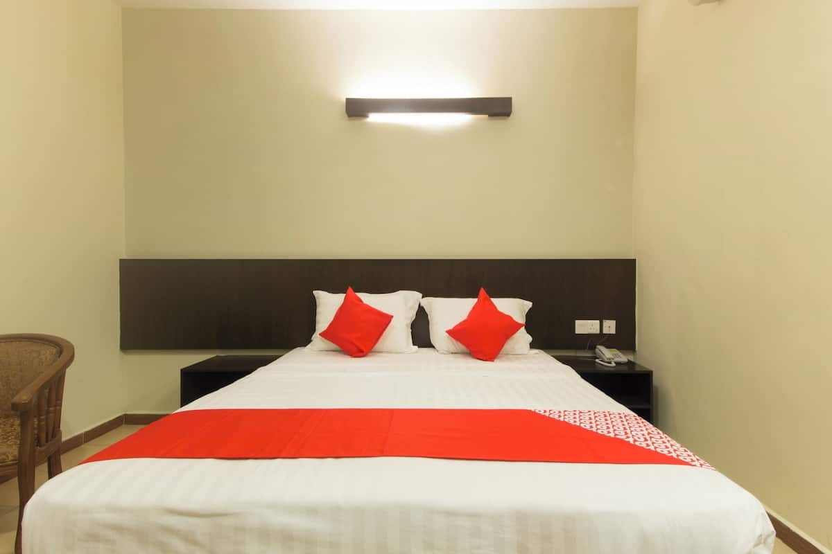 A hotel room with a large bed, two red pillows, a nightstand with a phone, and a wall-mounted light.