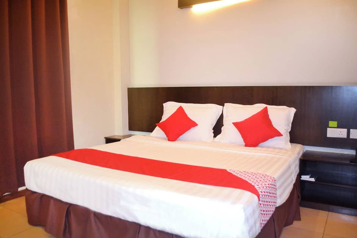A hotel room with a large bed, red and white bedding, a wooden headboard, and a nightstand with a lamp.