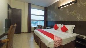 Een hotelkamer met een bed, een bureau, een stoel en een raam met uitzicht op gebouwen.