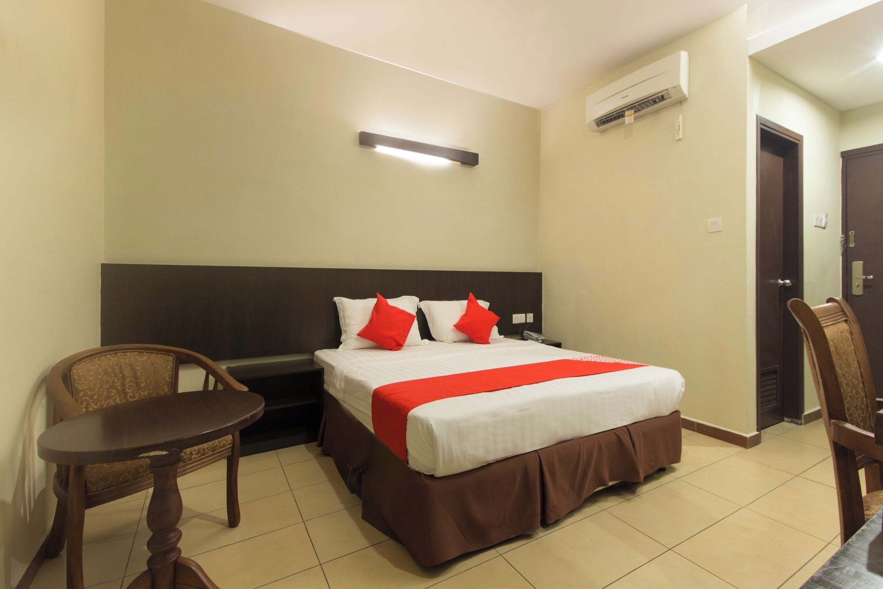 A hotel room with a bed, a chair, a small table, and an air conditioning unit.