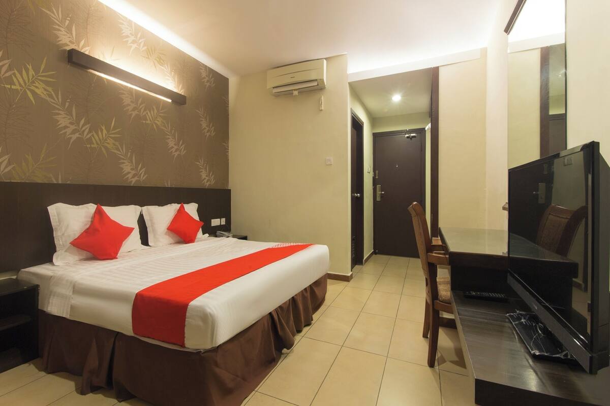 A hotel room with a bed, a TV, a desk, and an air conditioning unit.