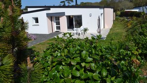 Ett modernt hus med en vit fasad, en uteplats med vita stolar och en trädgård med gröna växter.