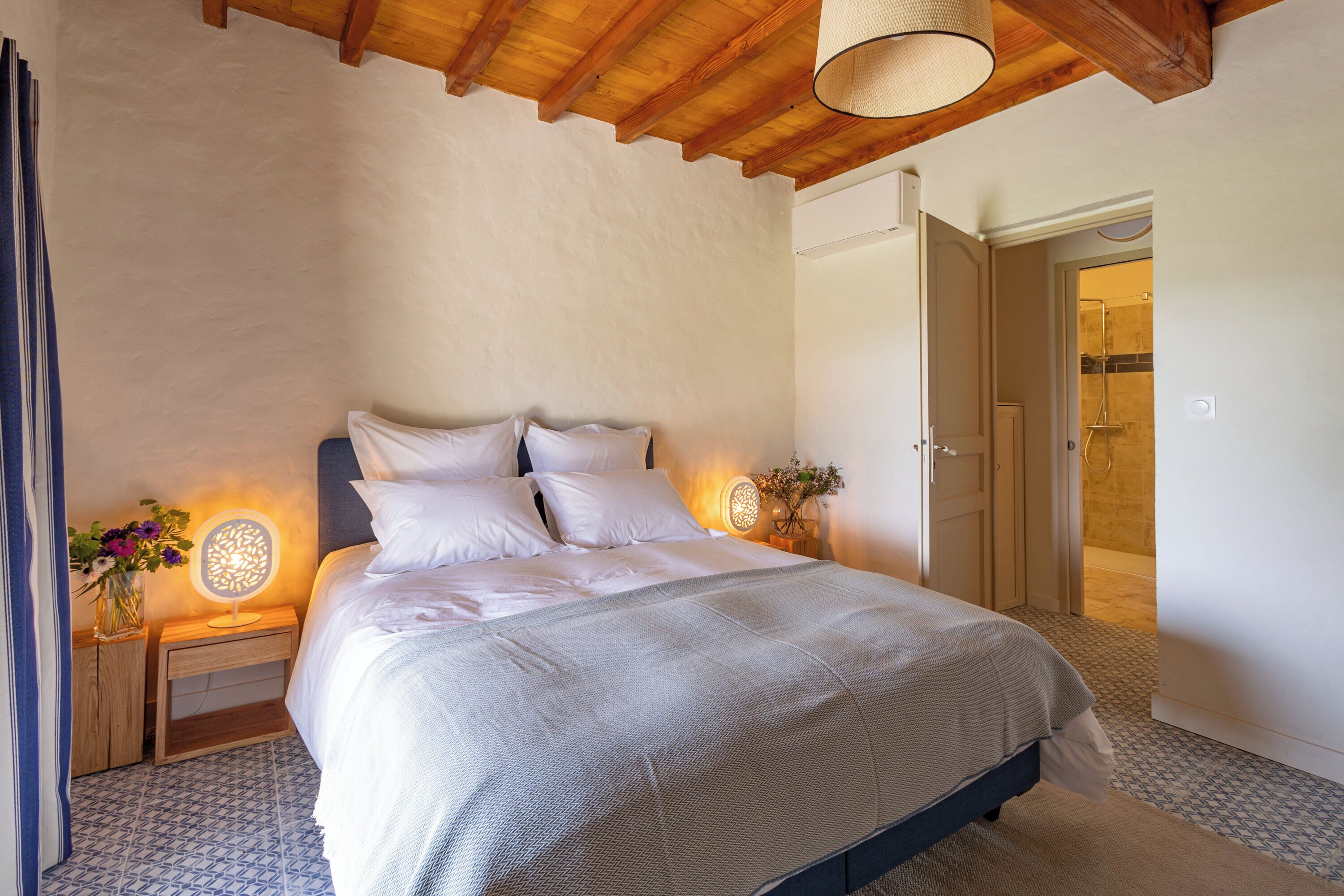 A bedroom with a large bed, wooden headboard, bedside lamps, and a door leading to a bathroom.