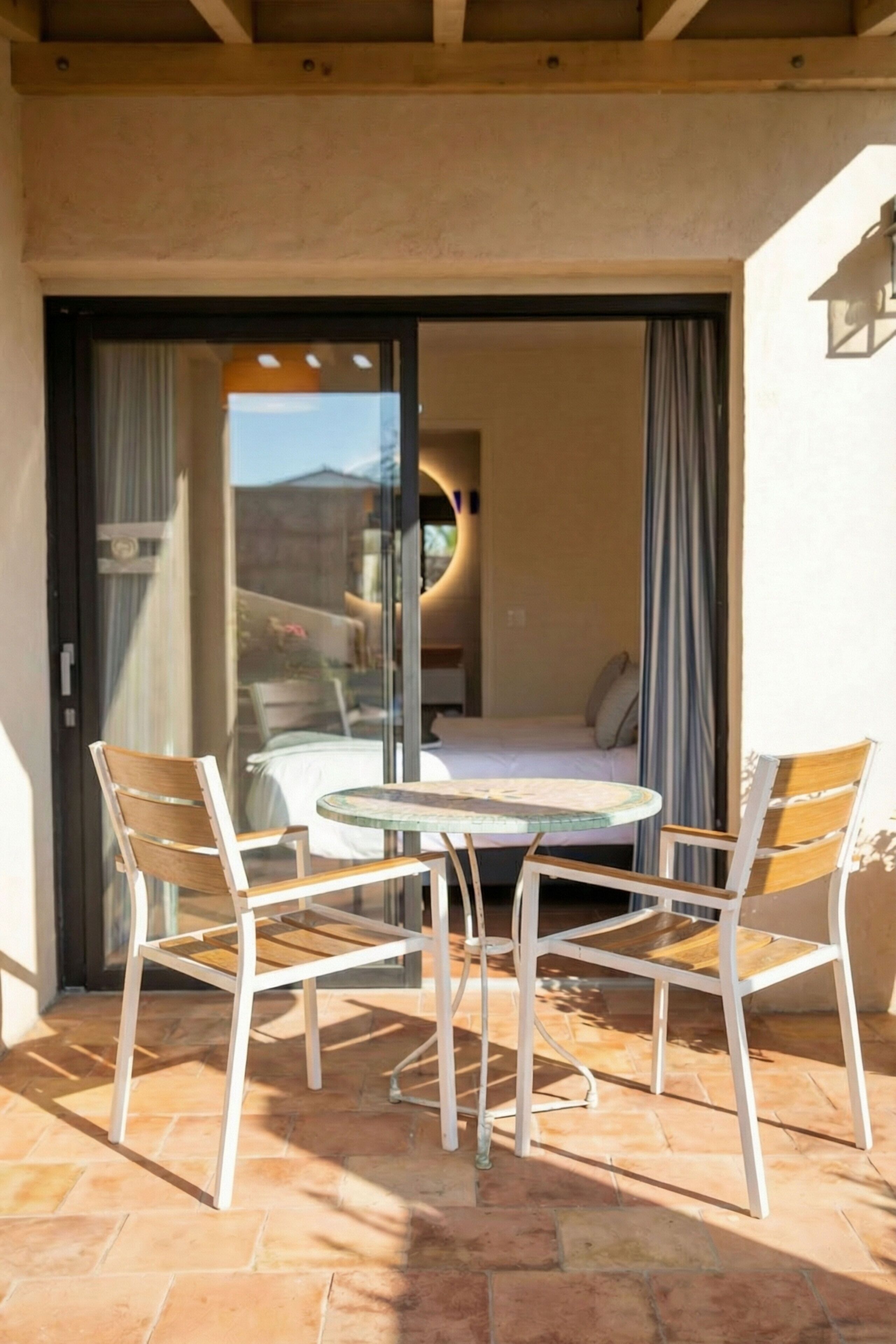 A patio with a table and chairs, a sliding glass door, and a bed visible through the door.