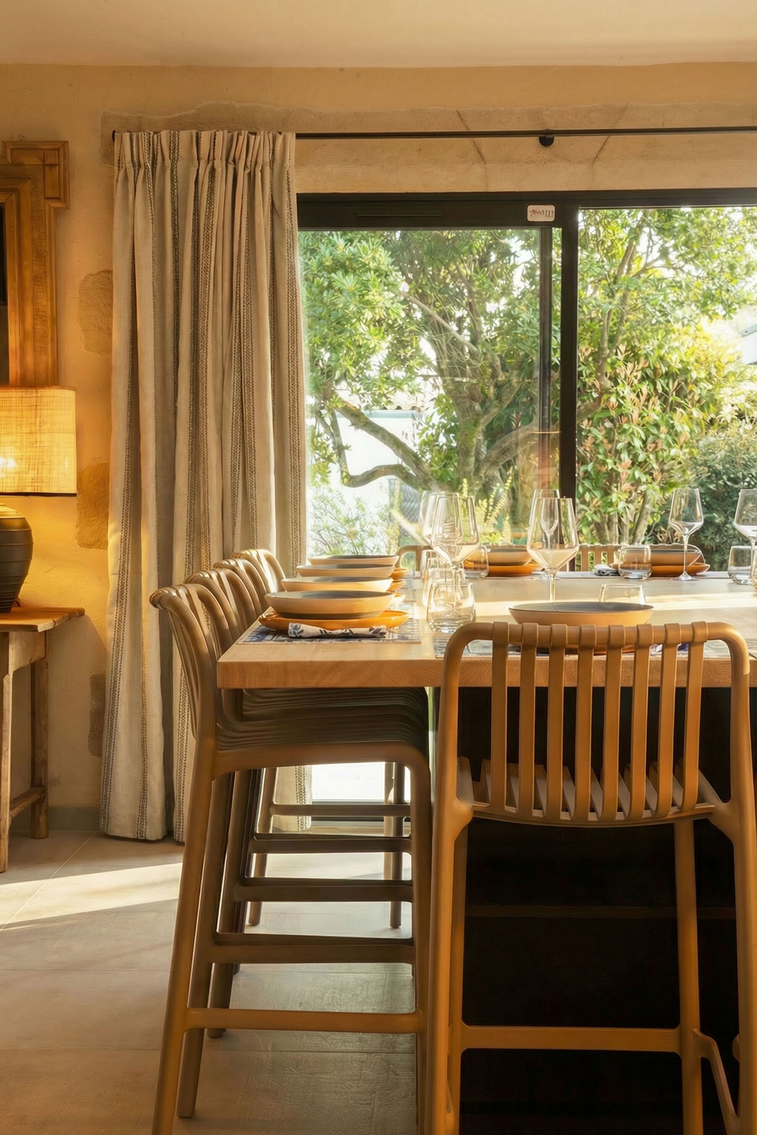 A dining area with a table set for four, chairs, a lamp, and a view through a window.