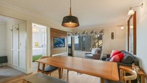A modern living room with a wooden dining table, a sofa with cushions, and a large window with a view. - Shamrock 1 - Mt Hotham (Hotham Heights)