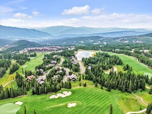 Un parcours de golf comprenant plusieurs bâtiments, un lac et des collines boisées environnantes.