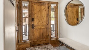 Een houten deur met een ruit, een bank en een ronde spiegel aan de muur.