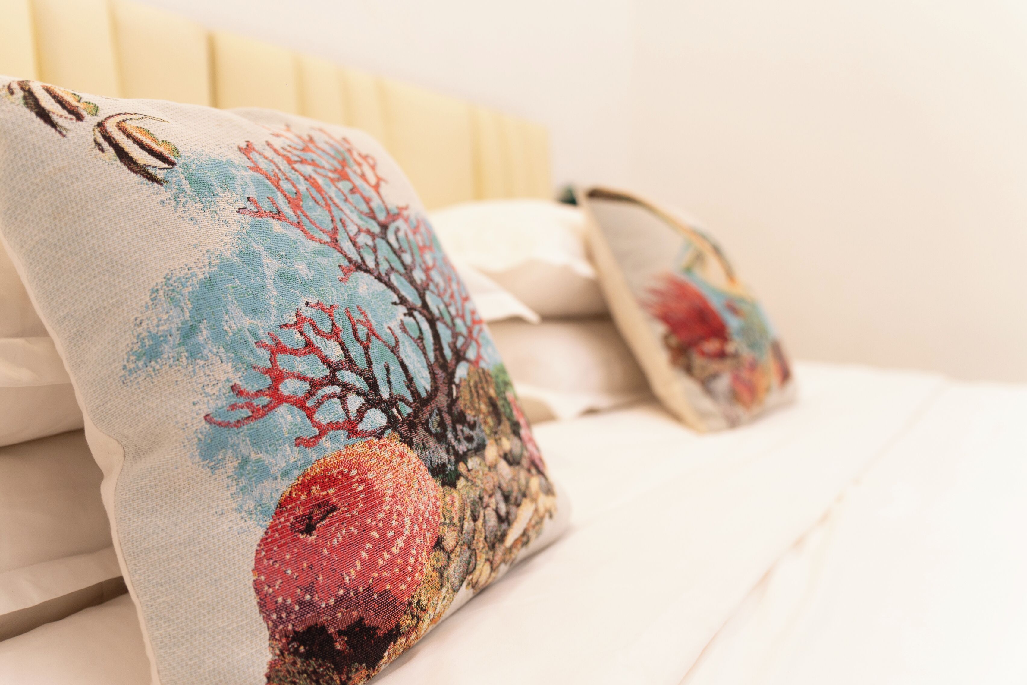 Una cama con sábanas blancas y dos almohadones decorativos con diseño de arrecife de coral.