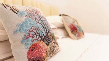 Una cama con sábanas blancas y dos almohadones decorativos con diseño de arrecife de coral.