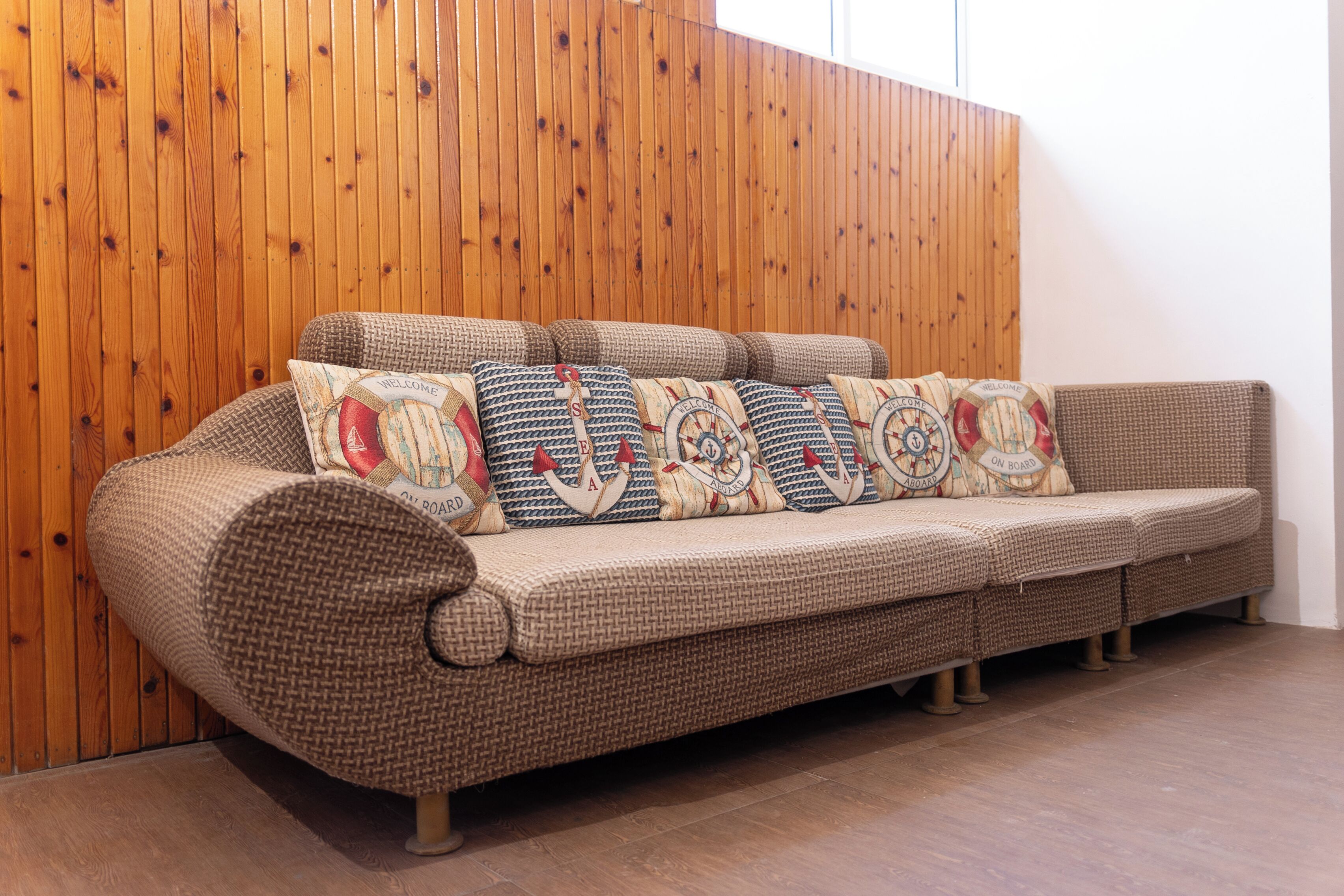Un canapé marron tissé, agrémenté de coussins à motifs, est placé contre un mur en bois.