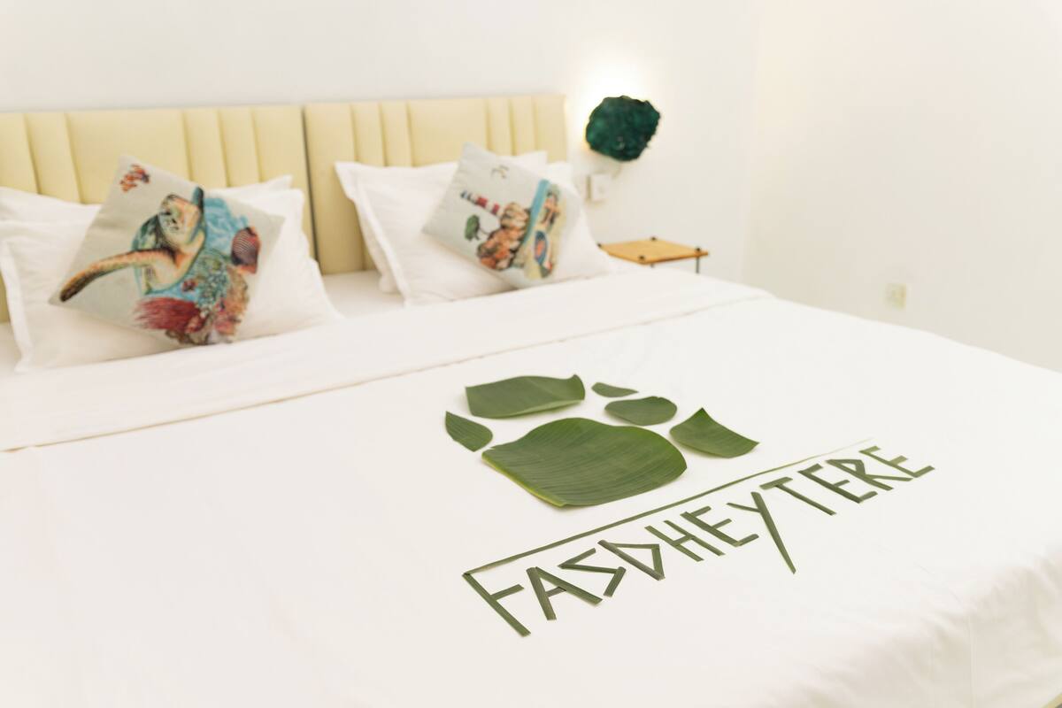 A bed with a white sheet featuring a green leaf design and the text "FASHEYTERE".