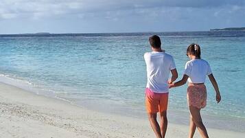 A couple walking on a beach with clear skies and calm sea.