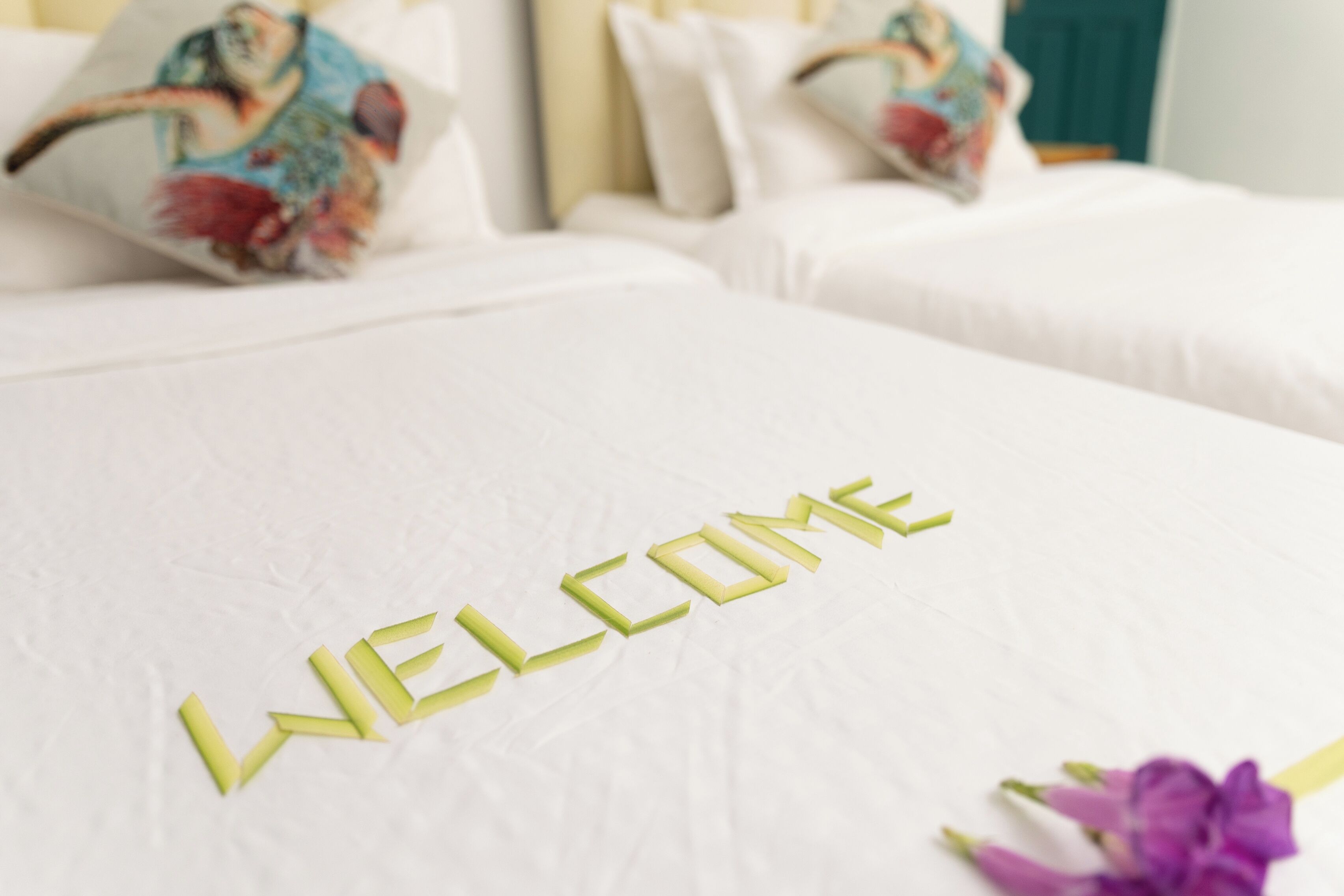 Ein Bett mit weißer Bettdecke und Kissen, und das Wort 'WELCOME' in gelben Buchstaben.