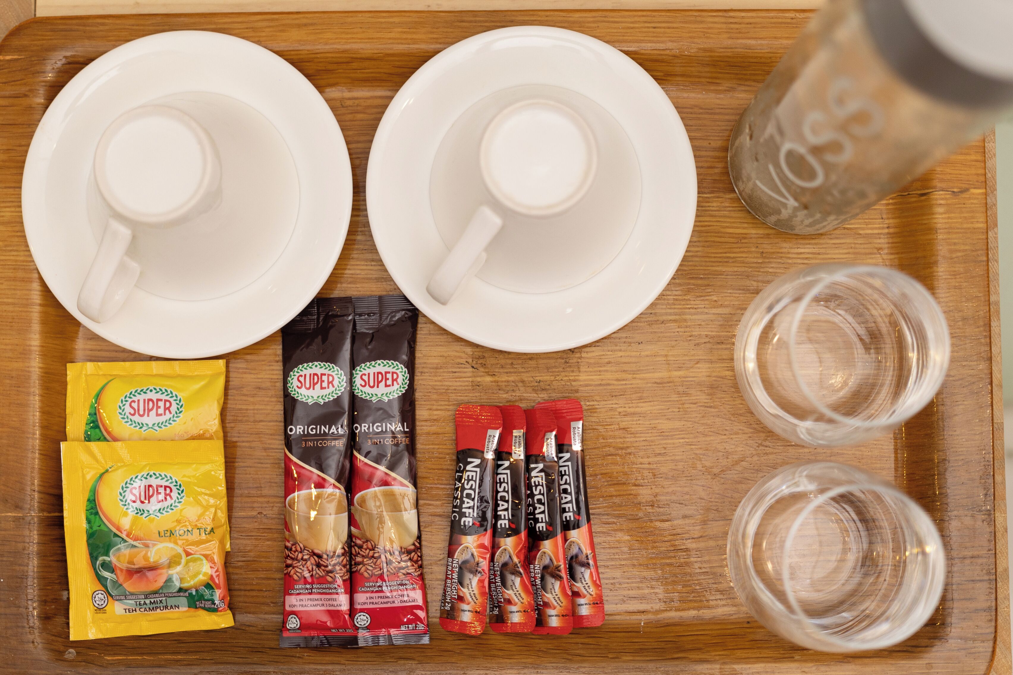 Una bandeja con dos tazas blancas, dos vasos, un salero y sobres de Nescafé y té Super Lemon.