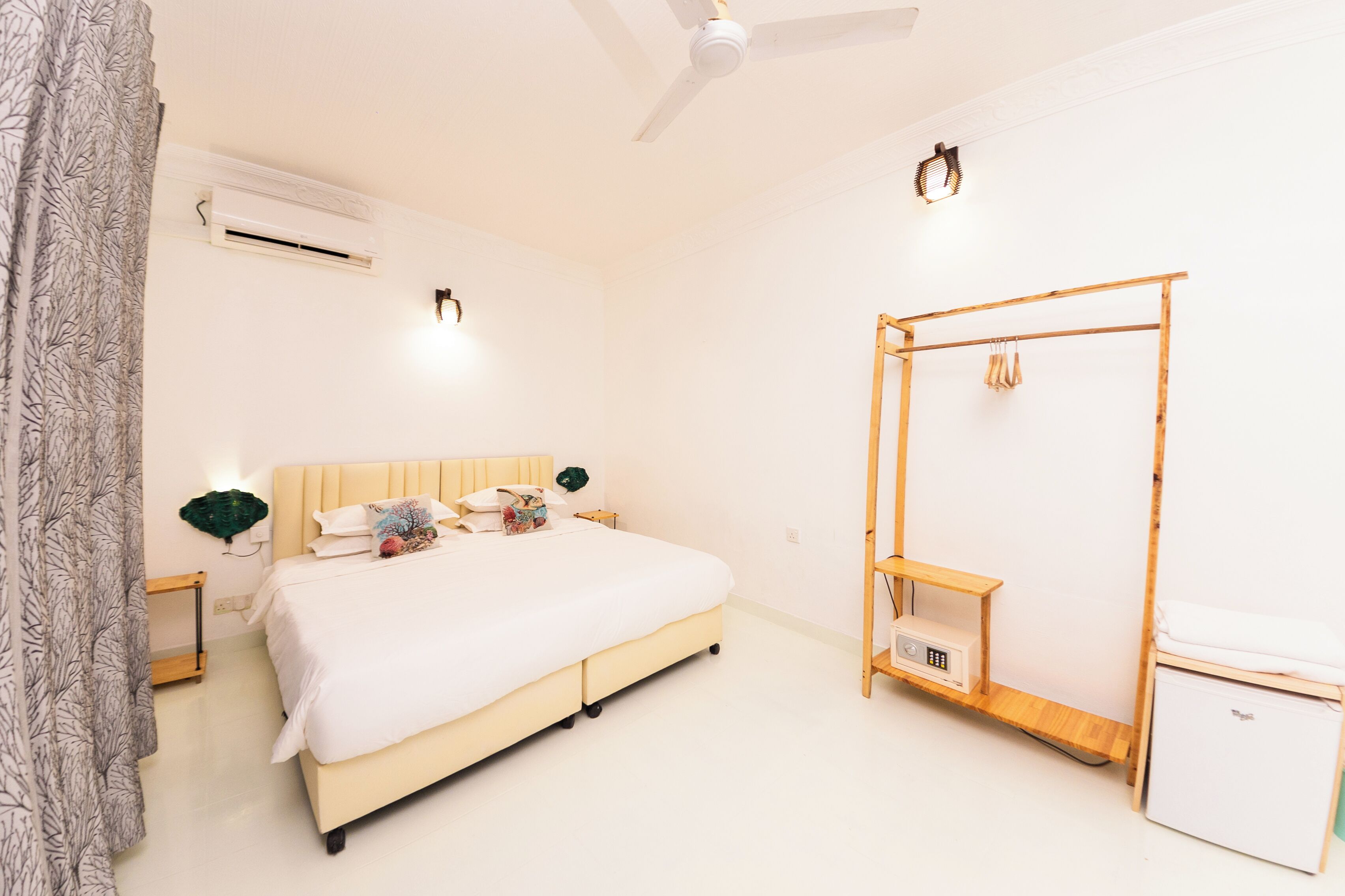 A bedroom with a bed, bedside tables, an air conditioning unit, a ceiling fan, a wardrobe, and a small cabinet.