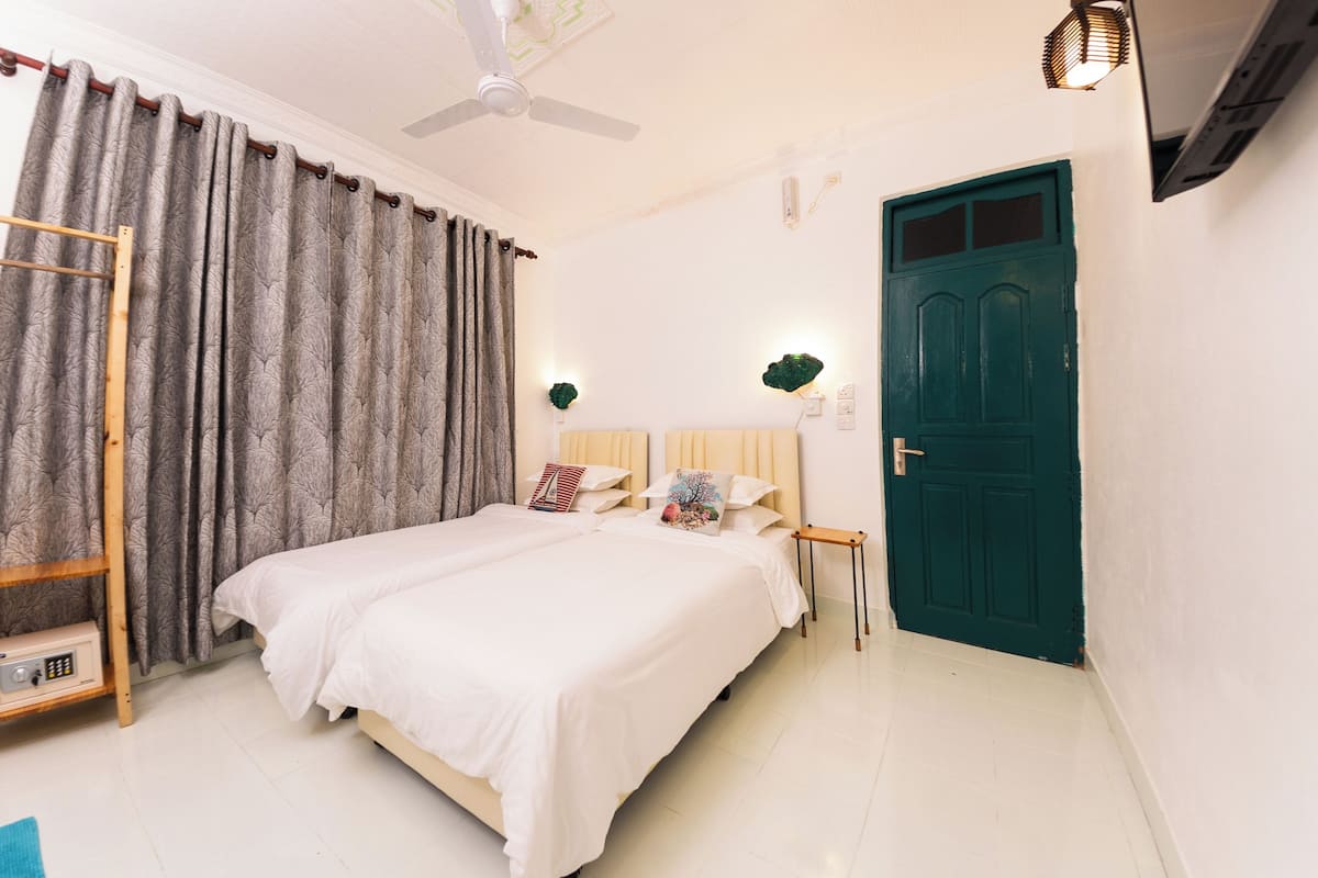 A neatly arranged bedroom with a bed, curtains, a door, and a ceiling fan.