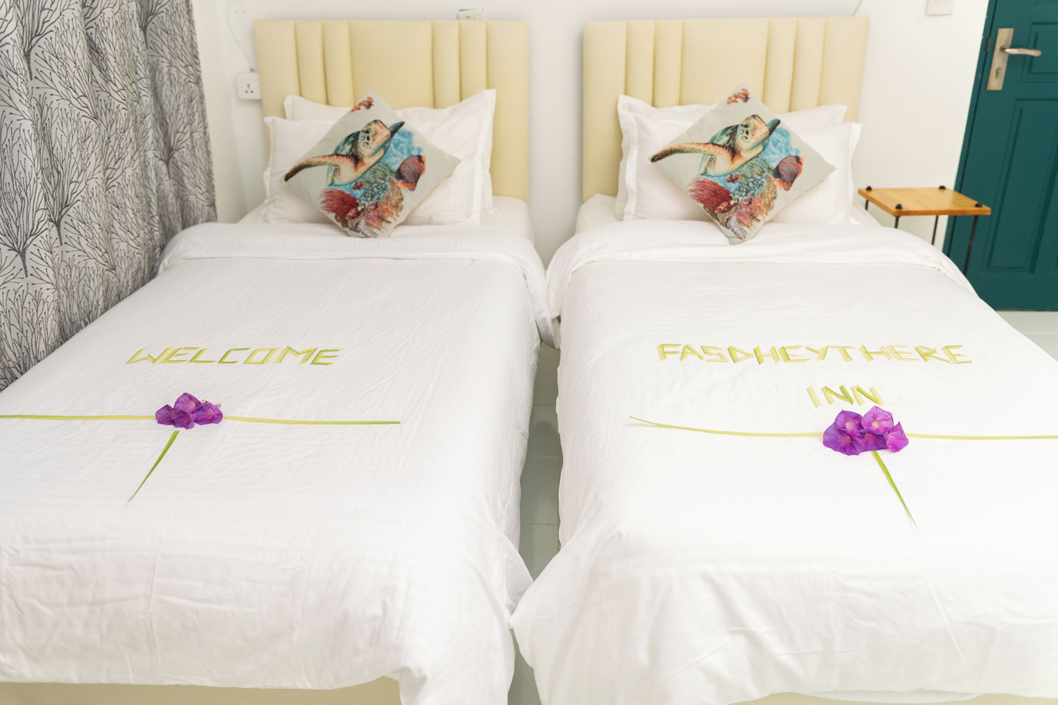 Due letti con lenzuola bianche e cuscini decorativi, ciascun letto con un'elegante composizione floreale e la scritta "WELCOME" e "FAMILY HERE INN" sul copripiumino.