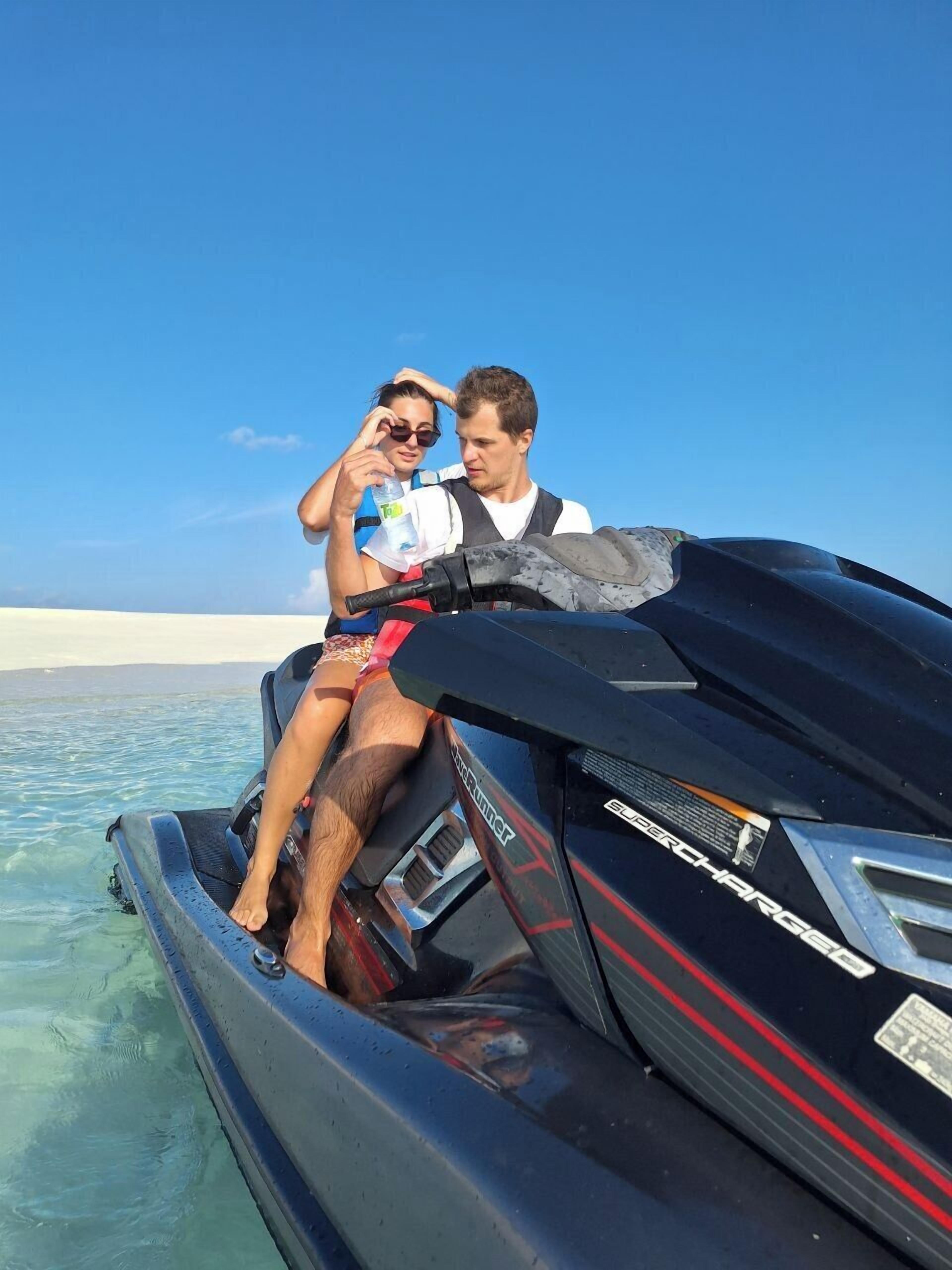 A jet ski with a person and a child on it, water in the background, and a clear sky.