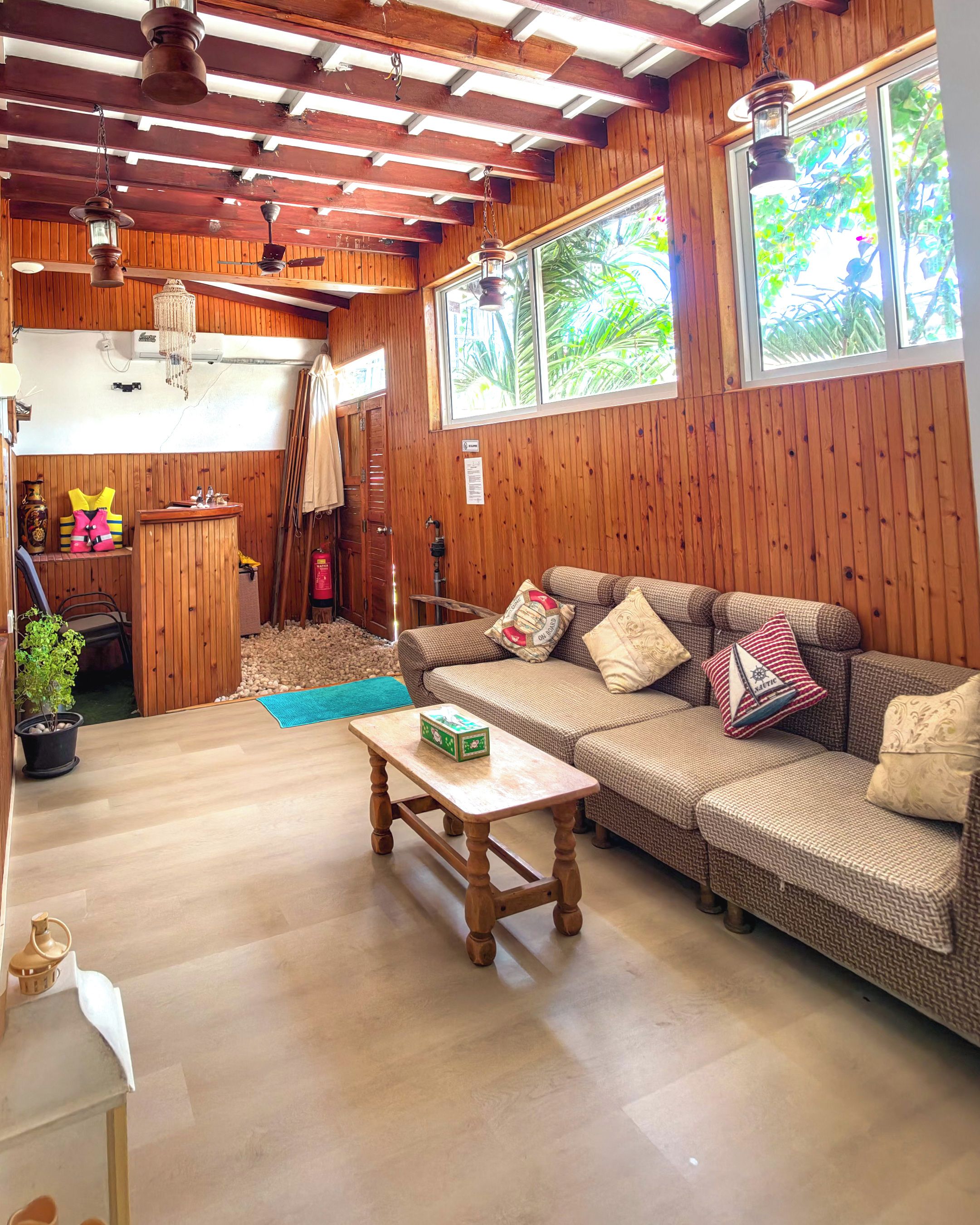 Een gezellige kamer met houten plafond, een bank, een tafel en een raam met uitzicht op groen.