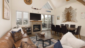 A spacious living room with a fireplace, a large TV, and a dining area with a view of the outdoors. - Ski-in, Ski-out Townhome with Private Hot Tub (Big Sky)