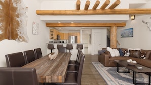 A spacious living area with a wooden dining table, leather chairs, a brown sofa, and a blue patterned rug. - Ski-in, Ski-out Townhome with Private Hot Tub (Big Sky)
