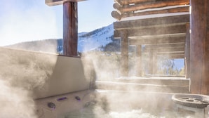 A hot tub with steam rising, surrounded by wooden structures and a mountainous backdrop. - Ski-in, Ski-out Townhome with Private Hot Tub (Big Sky)
