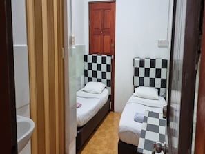 A small, narrow room with two beds, each with a checkered headboard, a wooden door, and a tiled floor. - Hotel O Jj Homestay (Miri)