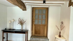 Eine Holztür mit Fensterfeldern, ein kleiner Tisch mit einer Vase getrockneter Blumen und ein weißer Nachttisch mit einer Vase.